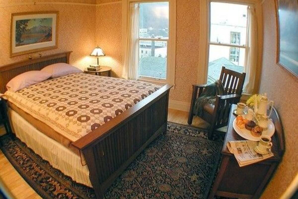 A hotel room with a bed, a chair, a table with breakfast, and a window with a view.