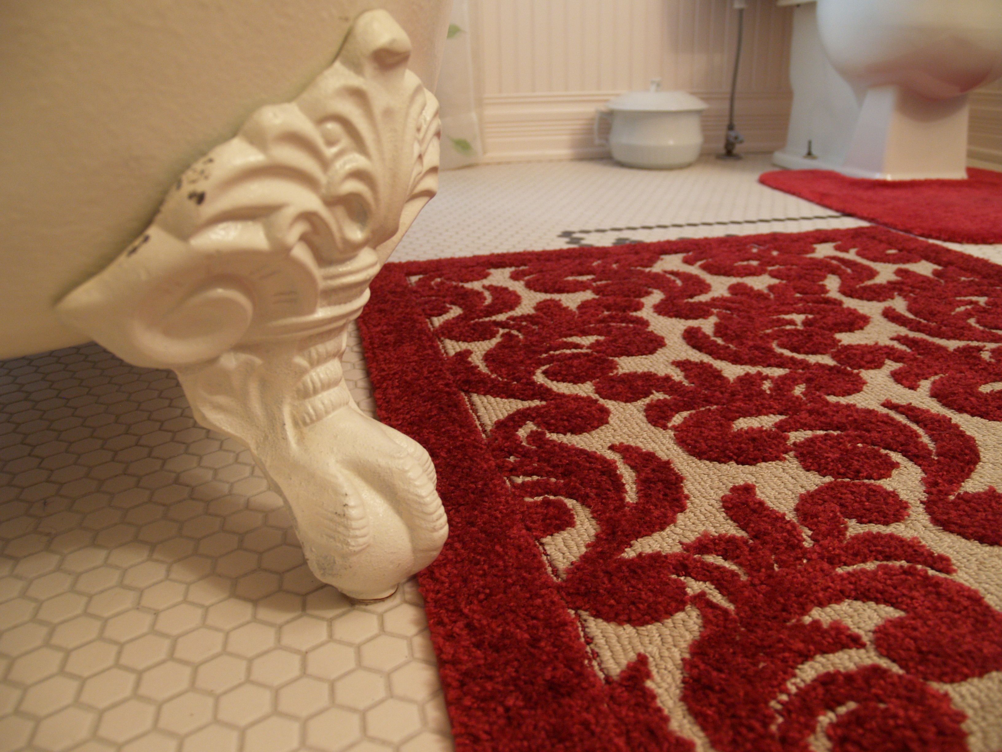 A bathroom with a white tiled floor, a red patterned rug, a white toilet, and a white pedestal sink.