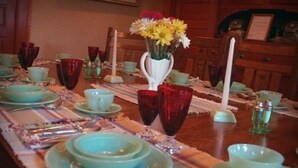 A dining table set with blue plates, red vases, and a vase of yellow flowers. - Alaskas Capital Inn Bed & Breakfast (Juneau)