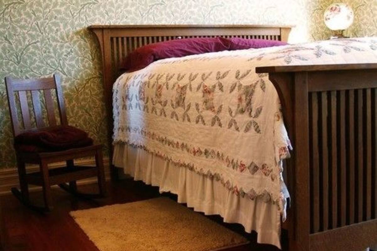 A bedroom with a wooden bed, a chair, and a patterned wall.