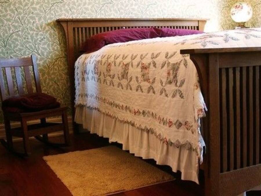 A bedroom with a wooden bed, a chair, and a patterned wall.