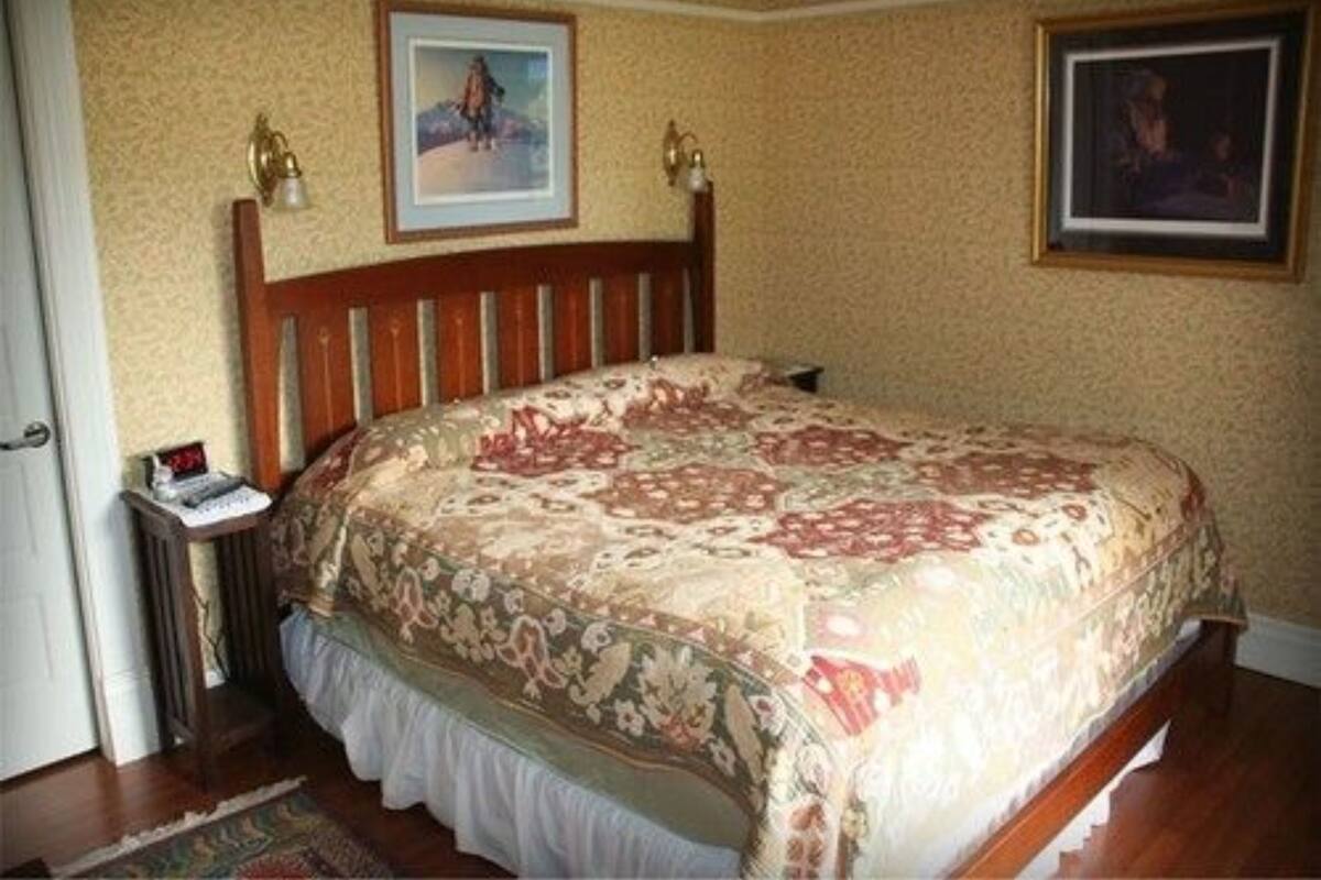 A bedroom with a wooden bed, floral bedspread, two wall-mounted lamps, and two framed pictures.