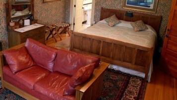 Un dormitorio con una cama de madera, un sofá de cuero rojo, una mesita de noche de madera y un espejo.