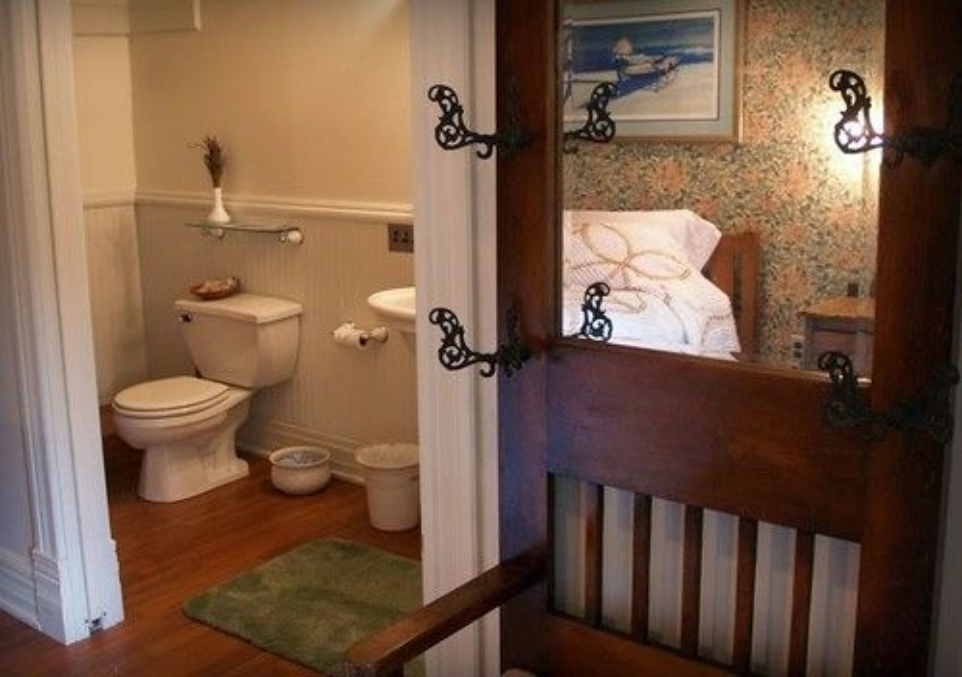 Une salle de bain avec des toilettes, un bidet et un petit lavabo. La porte est en bois et possède une poignée en métal.
