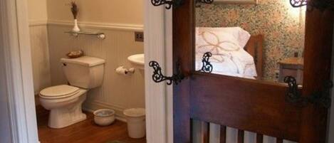 Une salle de bain avec des toilettes, un bidet et un petit lavabo. La porte est en bois et possède une poignée en métal.