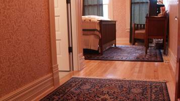 A hallway with a patterned carpet leading to a bedroom with a bed and a nightstand.