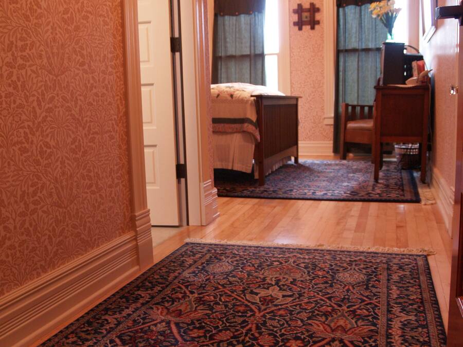 A hallway with a patterned carpet leading to a bedroom with a bed and a nightstand.