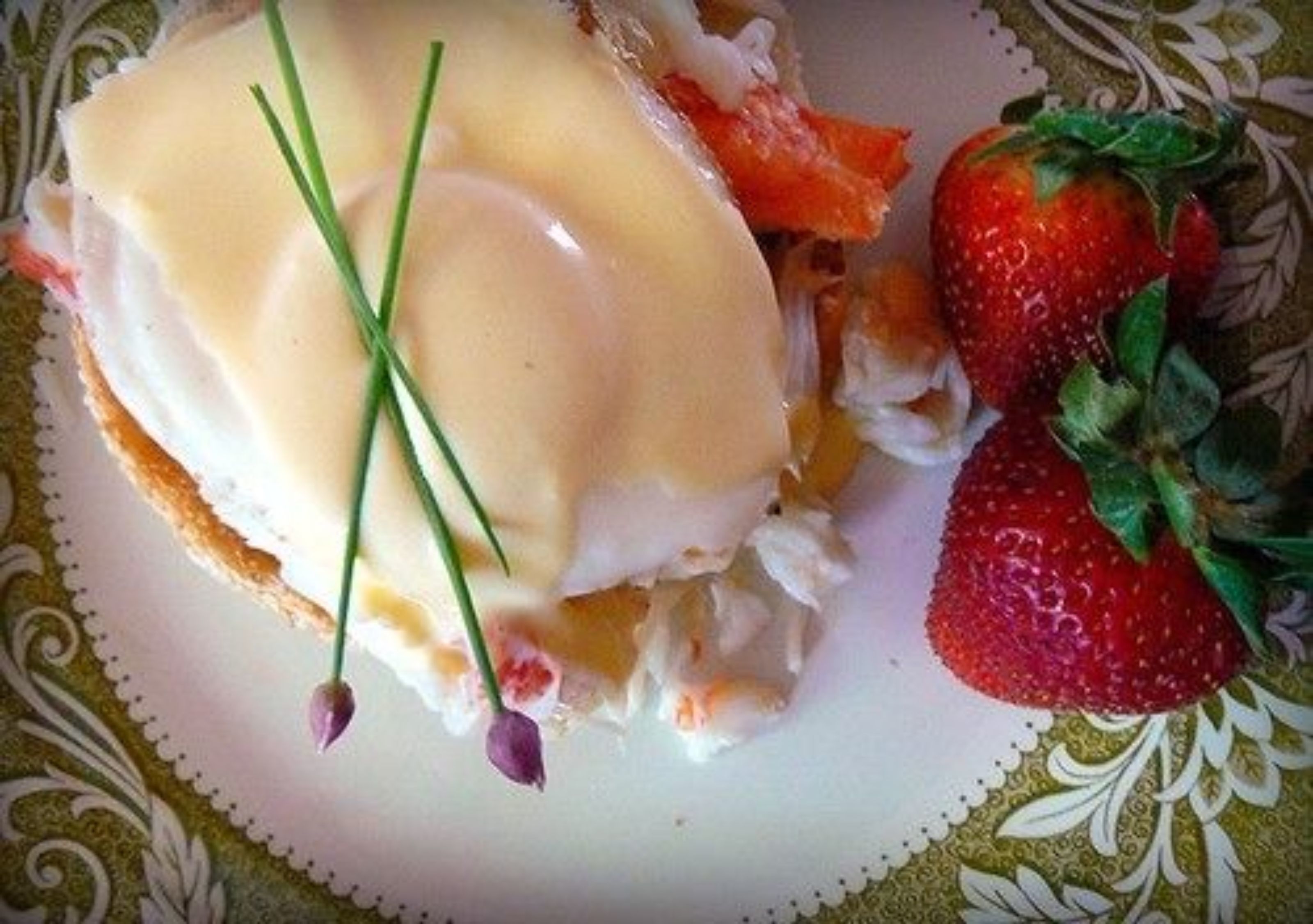 Un plato con un guiso que parece ser una tortilla de mariscos, adornada con cebollines, acompañada de una fresa.