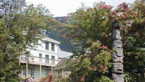 A two-story building with a balcony, surrounded by lush greenery and flowering plants. - Alaskas Capital Inn Bed & Breakfast (Juneau)