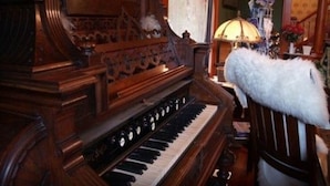 A grand piano with intricate woodwork and a plush white fur chair. - Alaskas Capital Inn Bed & Breakfast (Juneau)