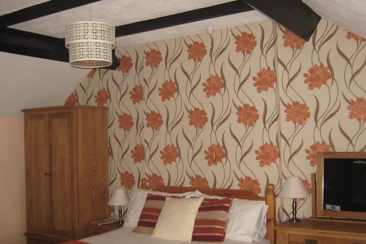 Een slaapkamer met een bed, twee nachtkastjes, een houten garderobe en behang met een bloemenmotief.
