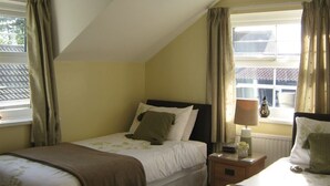 Een slaapkamer met een enkel bed, een nachtkastje met een lamp en een raam met gordijnen.