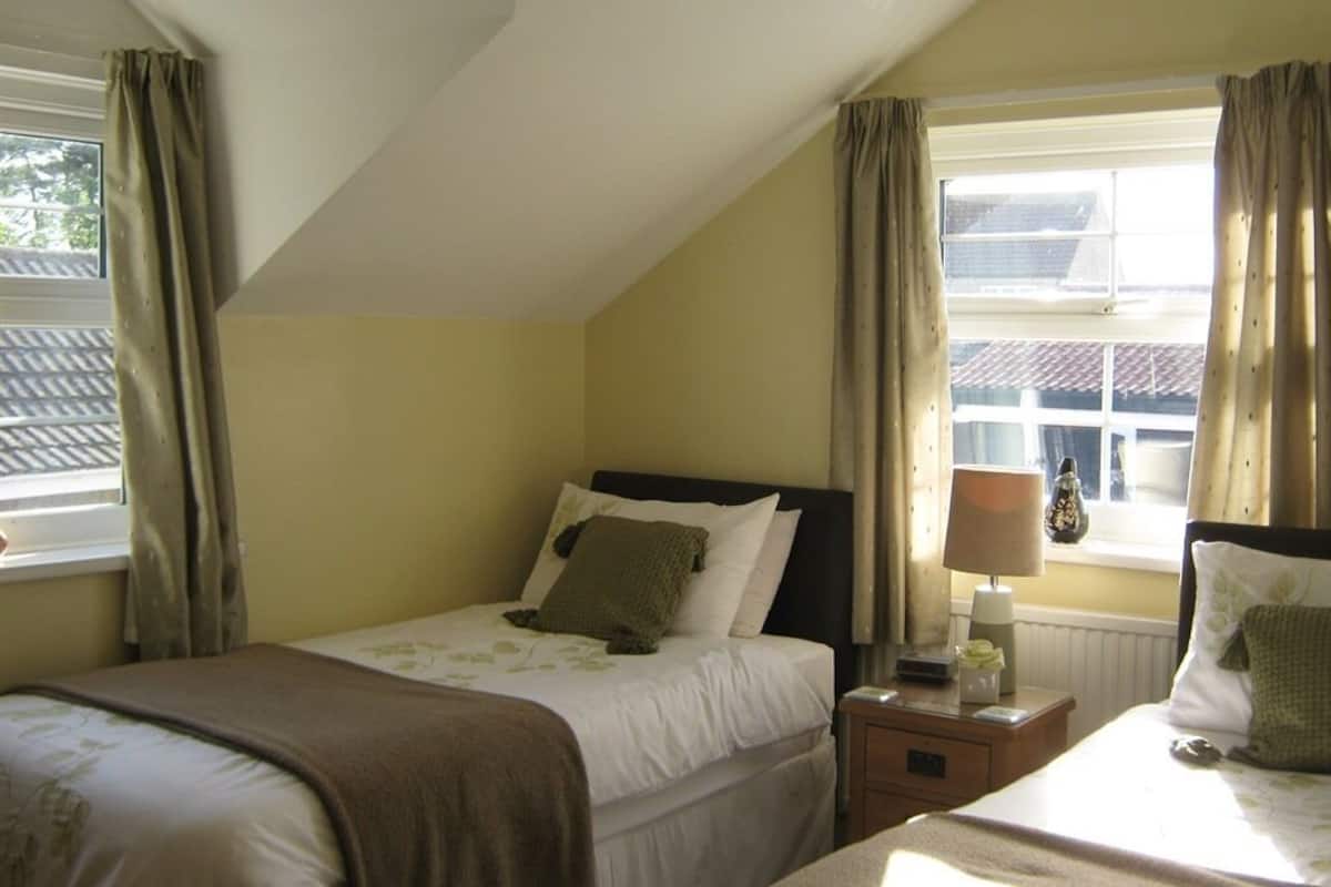 Een slaapkamer met een enkel bed, een nachtkastje met een lamp en een raam met gordijnen.