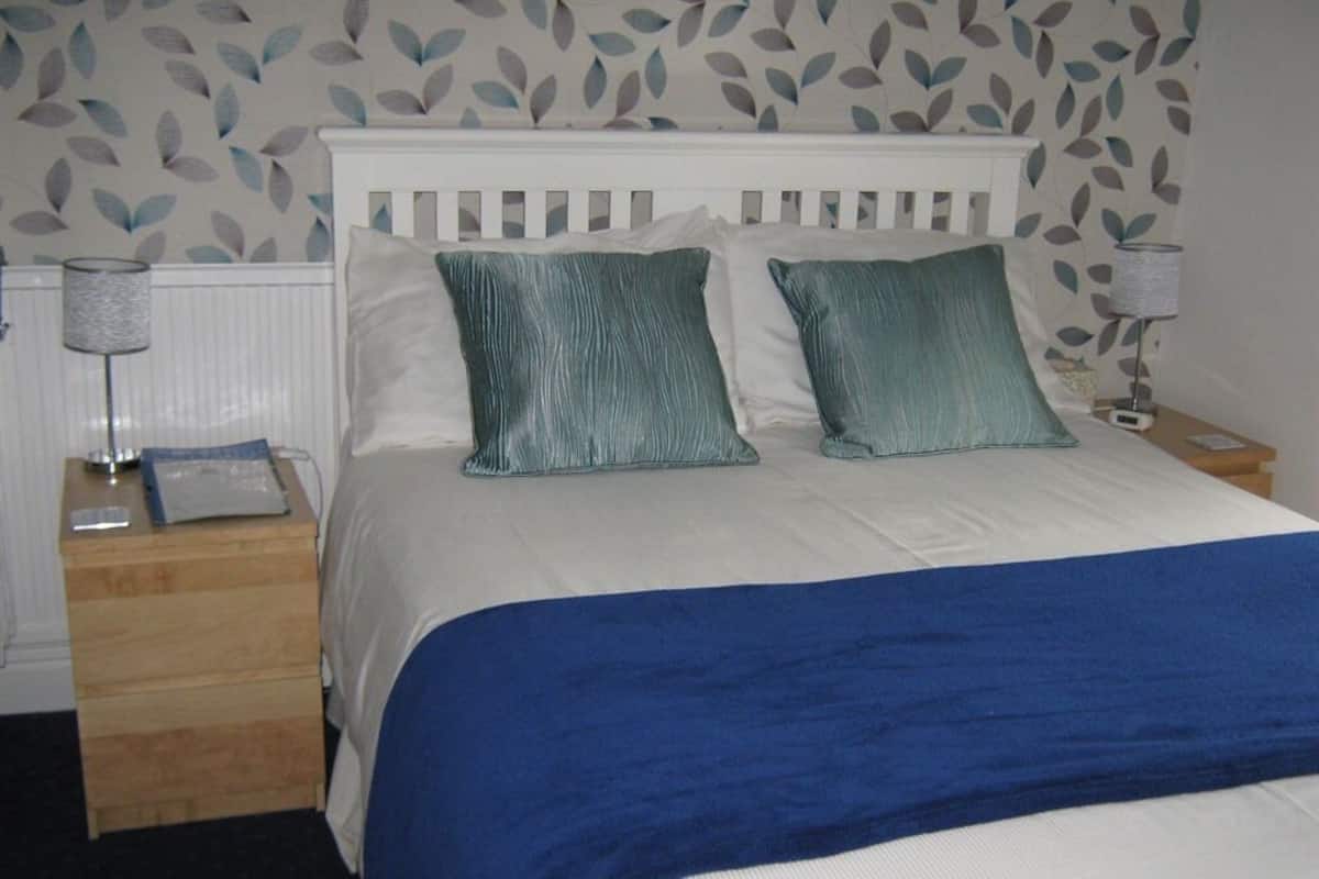 Een bed met een wit hoofdbord, twee turquoise kussens en een blauwe deken.
