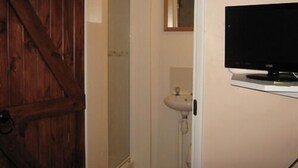 Een badkamer met een houten deur, een witte wastafel en een televisie aan de muur.