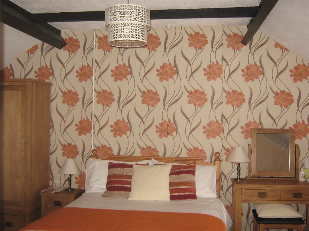 Een slaapkamer met een bed, nachtkastjes, een houten dressoir, een bureau met spiegel en een hanglamp.