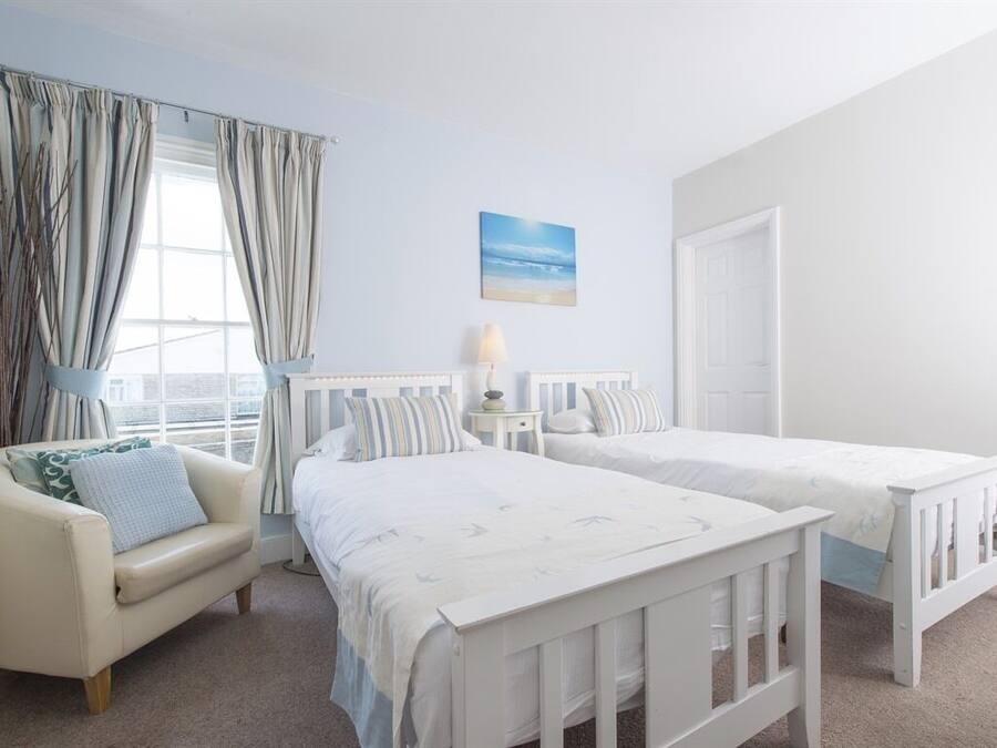 A bedroom with two single beds, a bedside table with a lamp, a chair, and a window with curtains.