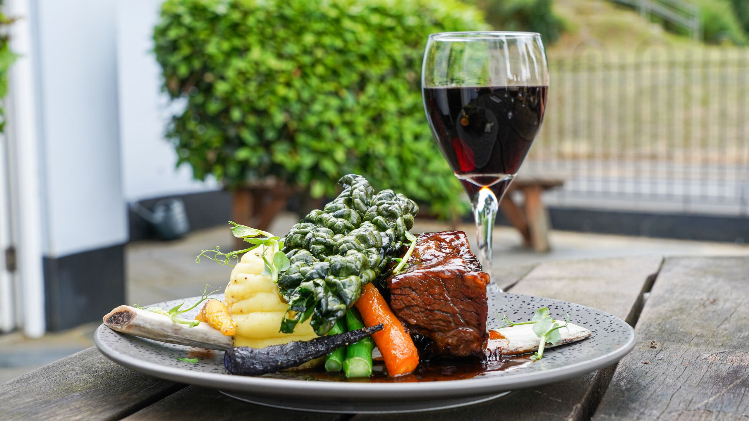 Prato de comida com um copo de vinho tinto sobre uma mesa de madeira.