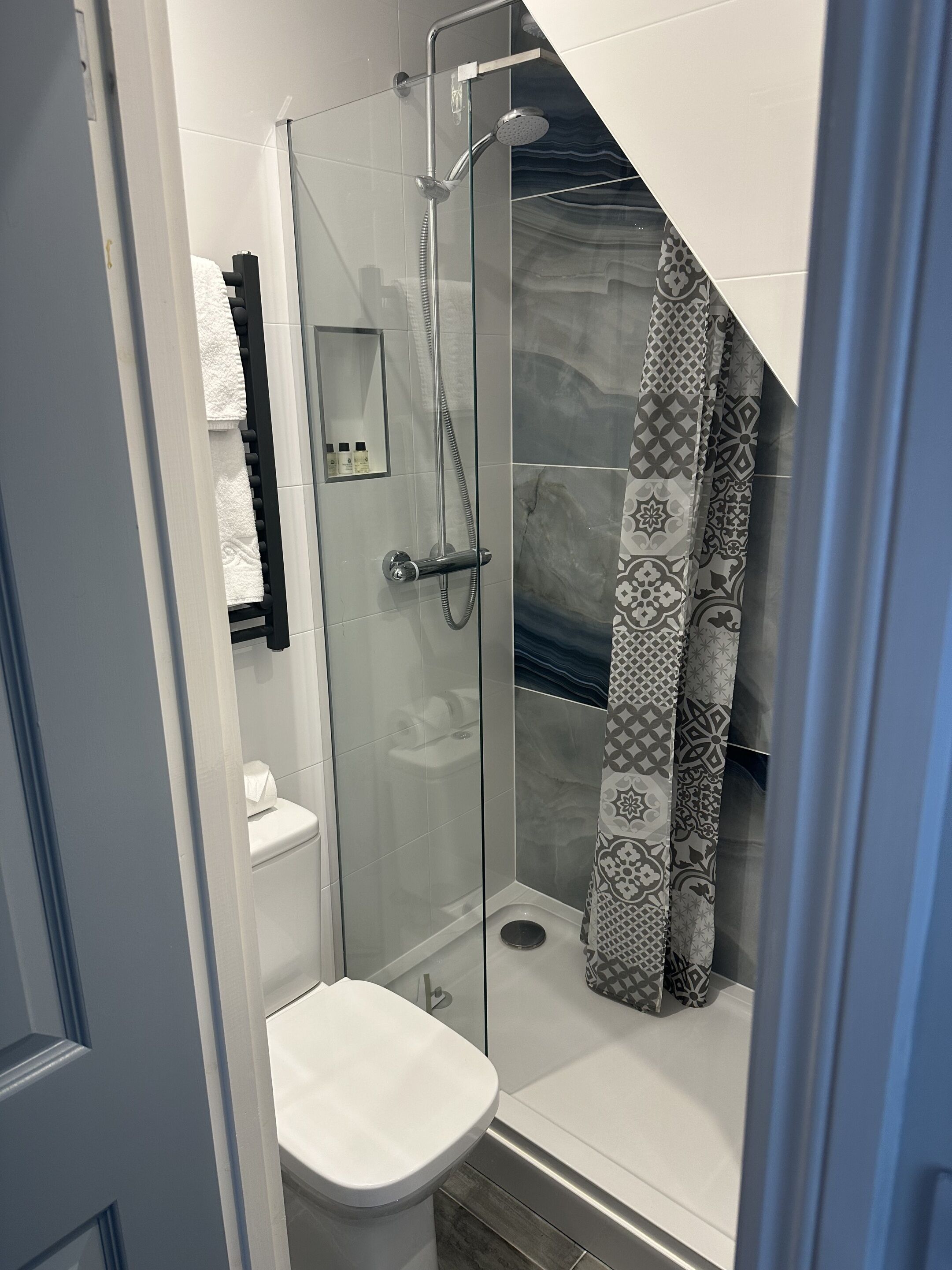 Un baño moderno con ducha de vidrio, inodoro y cortina de baño estampada.