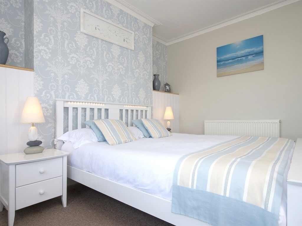 Een slaapkamer met een bed, nachtkastjes, een klok, een schilderij en een radiator.