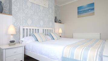 A bedroom with a bed, nightstands, a clock, a painting, and a radiator.