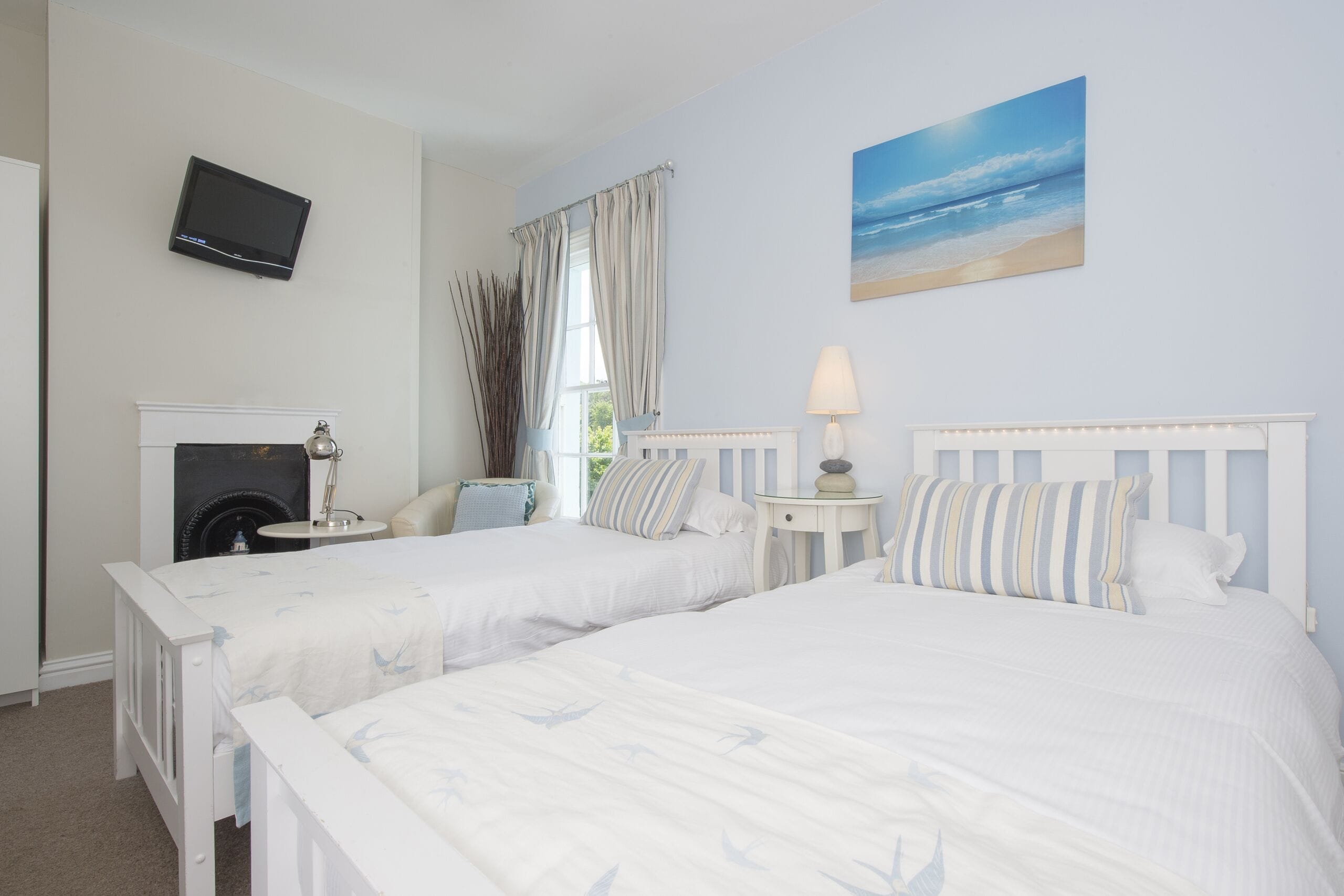 A bedroom with two beds, a television, a fireplace, and a beach view.