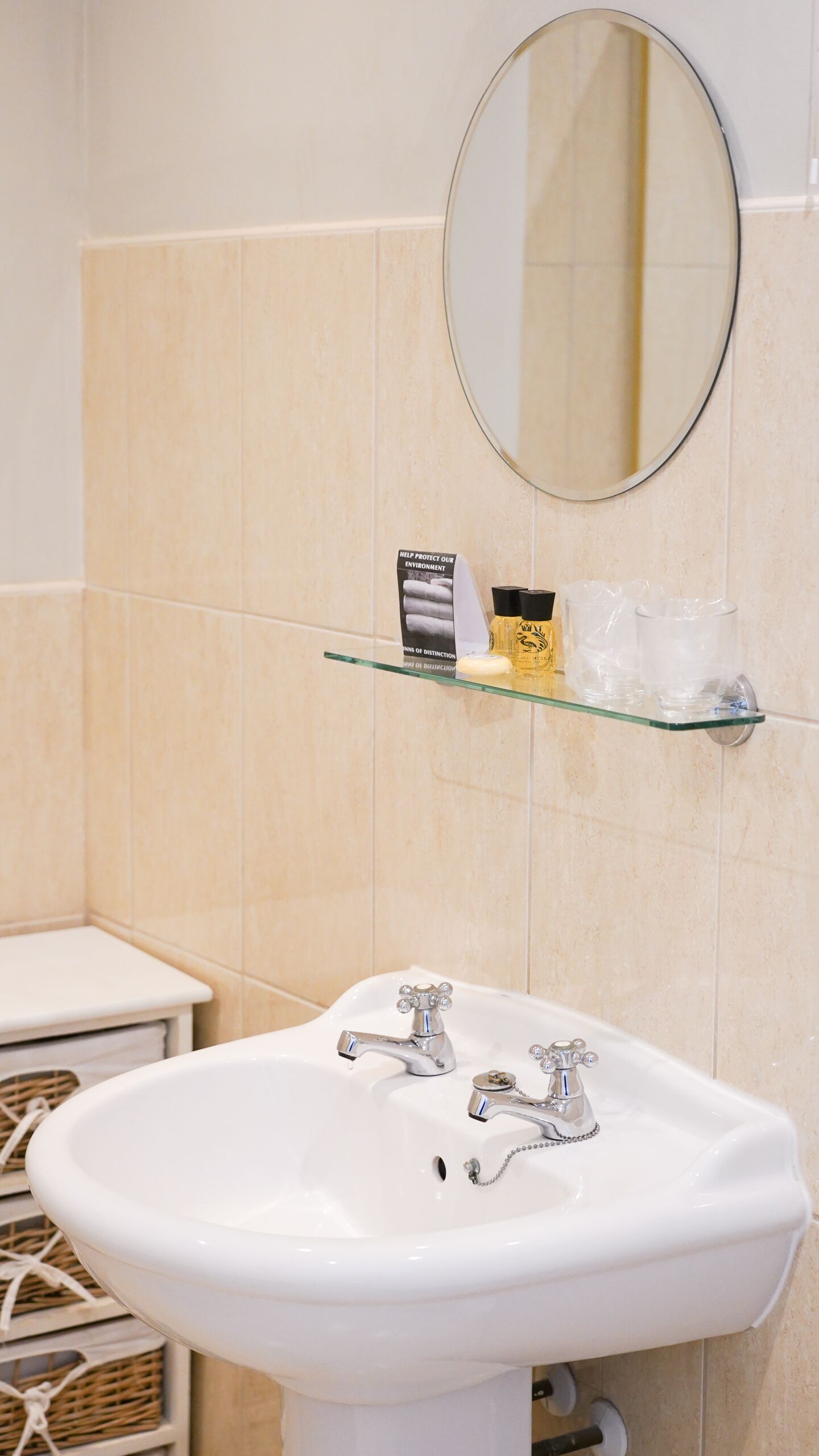 Un baño con un lavamanos blanco, dos grifos, un espejo y una repisa con artículos de aseo.