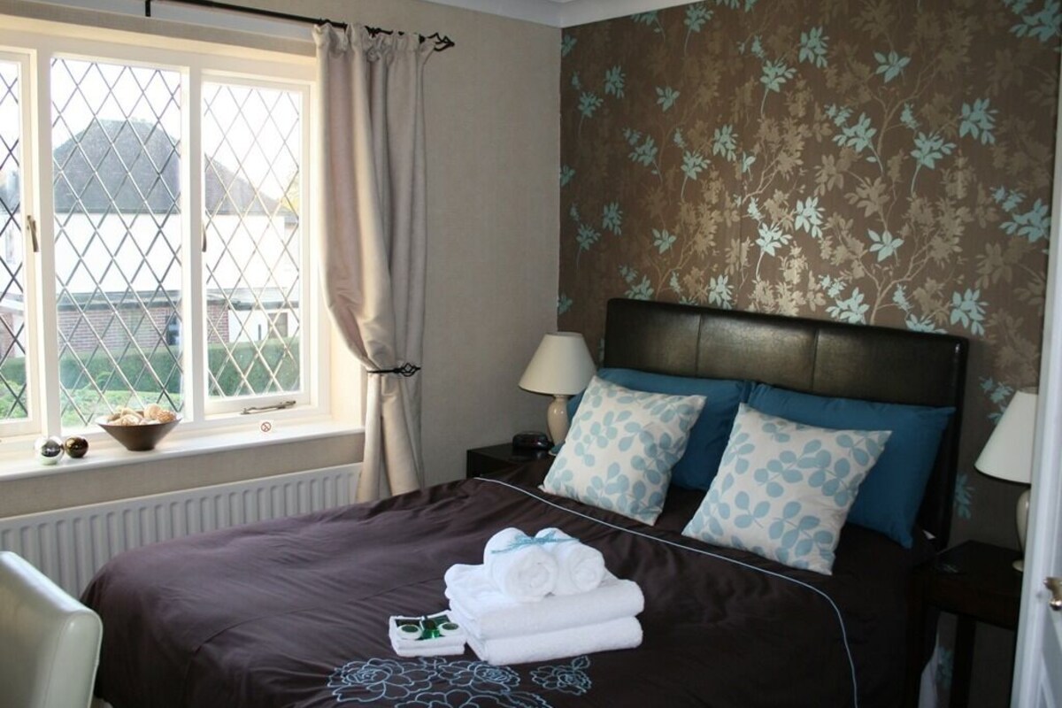 A bedroom with a bed, a window with curtains, a radiator, and a wall with a floral pattern.
