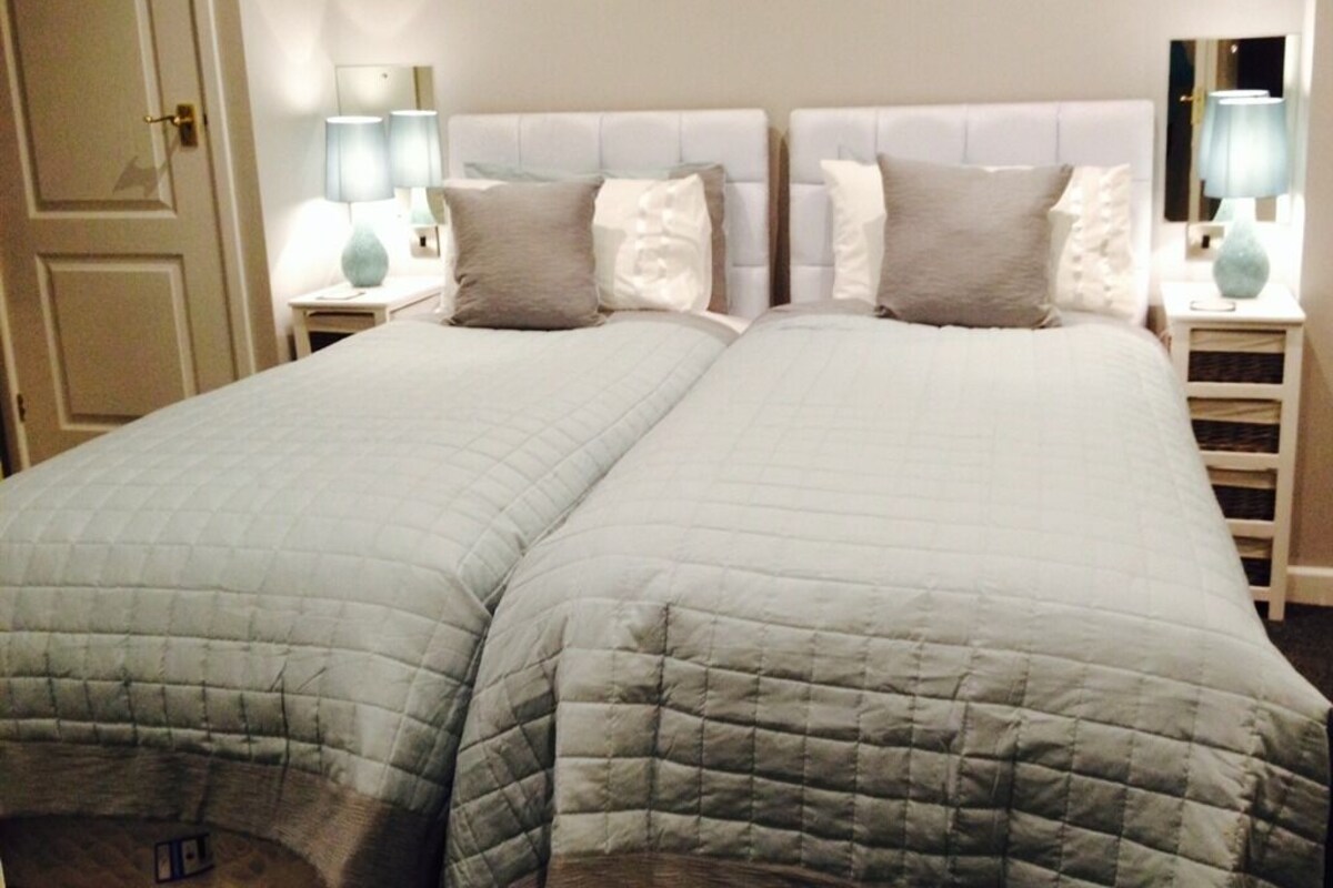 A double bed with a quilted grey duvet, two bedside tables with lamps, and a white door.