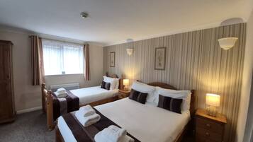 A hotel room with two beds, a window with curtains, a radiator, a wall-mounted light fixture, and a framed picture.