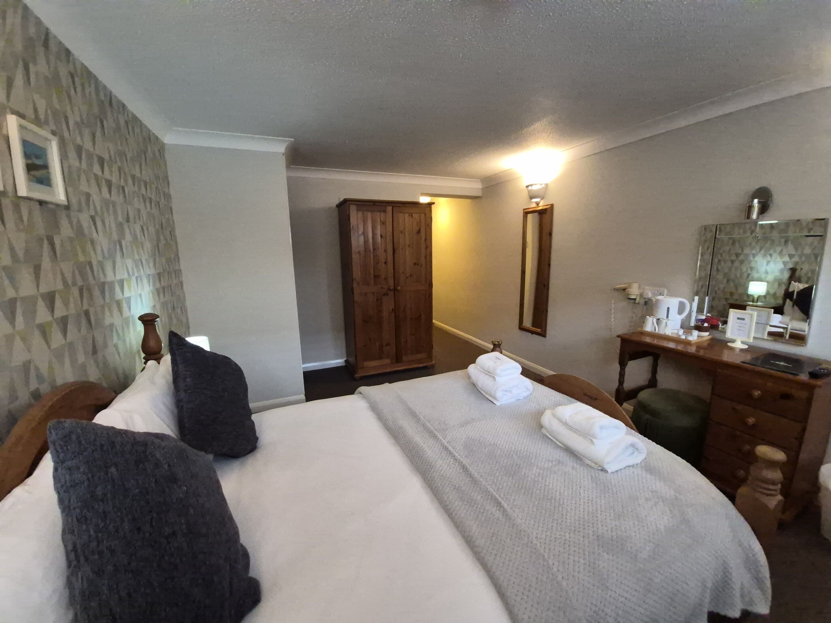 A hotel room with a bed, a desk, a mirror, and a wardrobe.