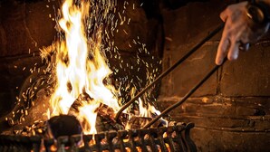 A close-up of a hand adjusting a metal grate over a fire. - The Heath Inn (Leighton Buzzard)