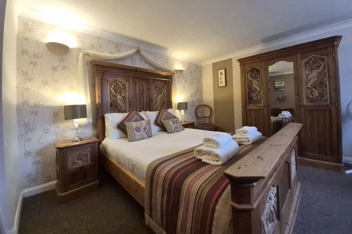 A neatly arranged bedroom with a large bed, two bedside tables with lamps, a wooden dresser, and a mirror.