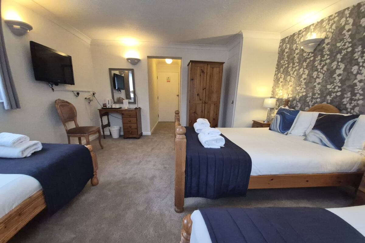A hotel room with two single beds, a desk with a chair, a television, and a wooden wardrobe.