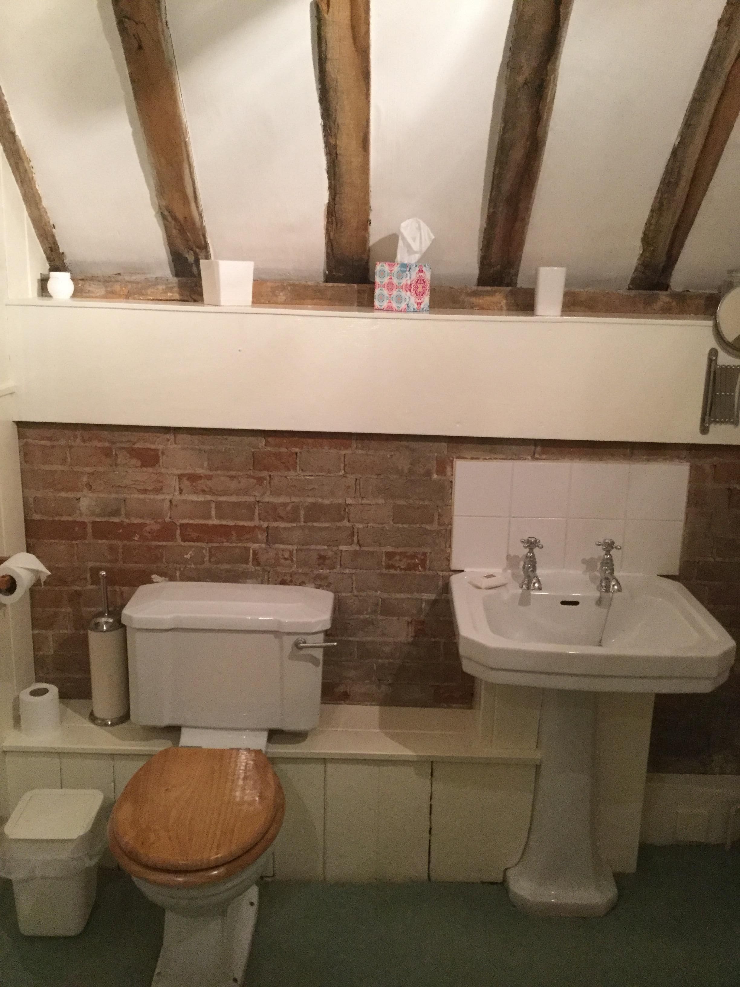 A bathroom with a toilet, sink, and a shelf above the sink.
