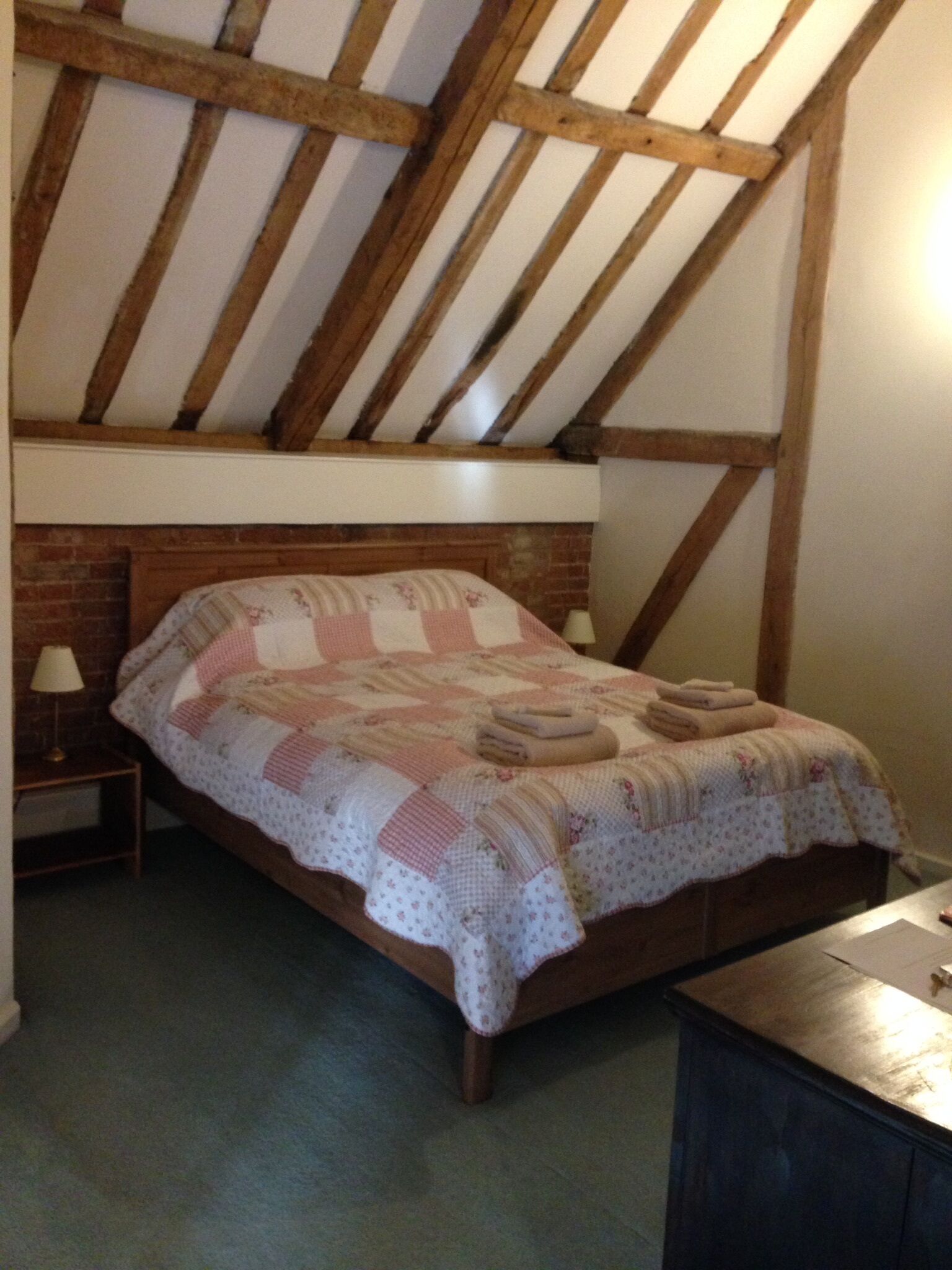 Een slaapkamer met een houten bed, een sprei, een nachtkastje met een lamp en een bakstenen muur.