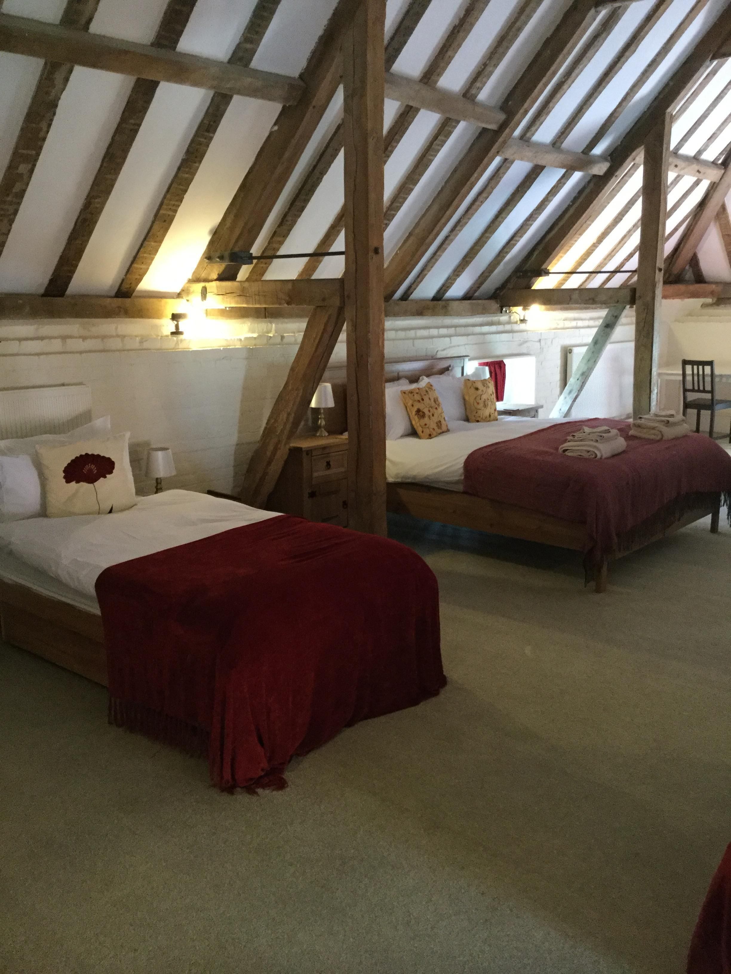 A bedroom with two beds, wooden beams, a sloped ceiling, and a brick wall.