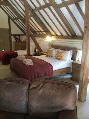 A cozy bedroom with a wooden ceiling, a large bed with floral pillows, a red blanket, and a wooden nightstand.