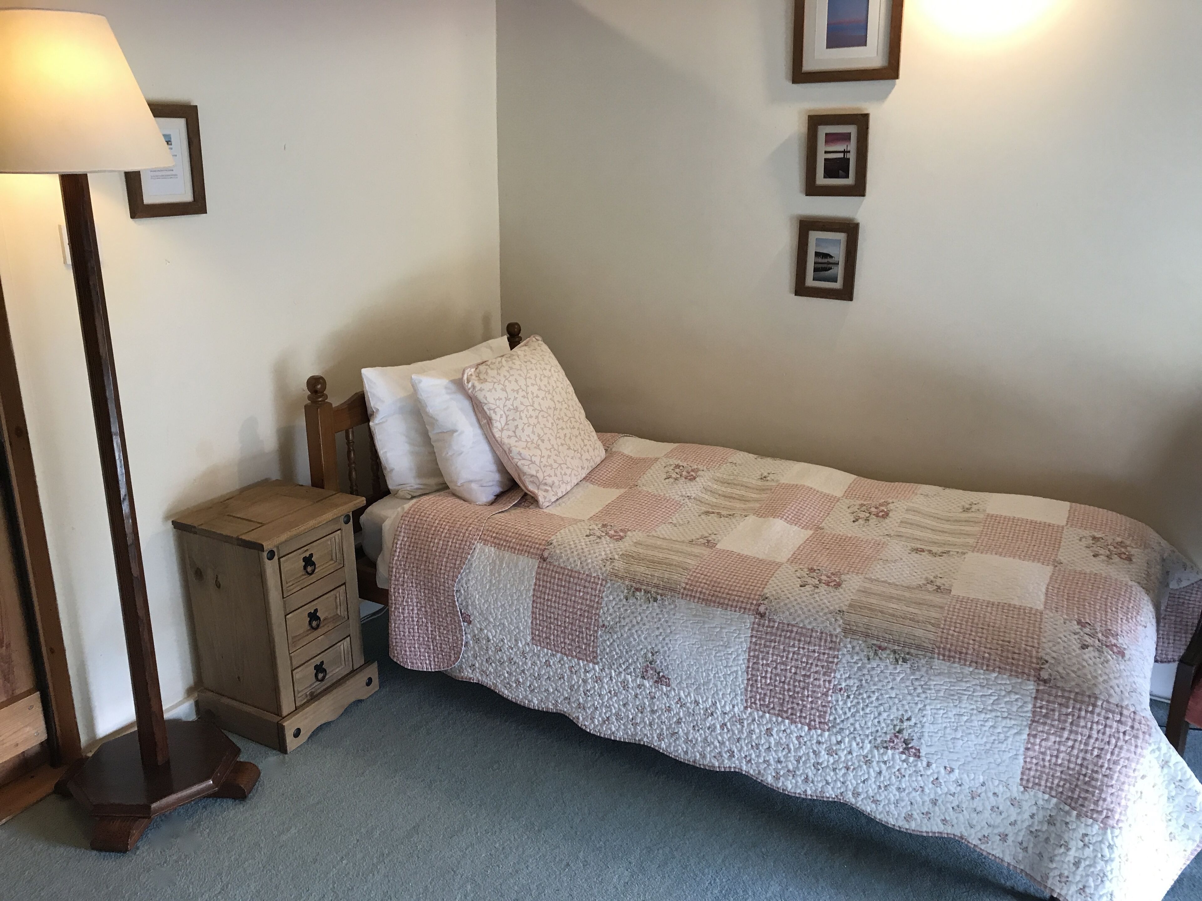 Un dormitorio con una cama individual, una mesita de noche, una lámpara y tres cuadros en la pared.