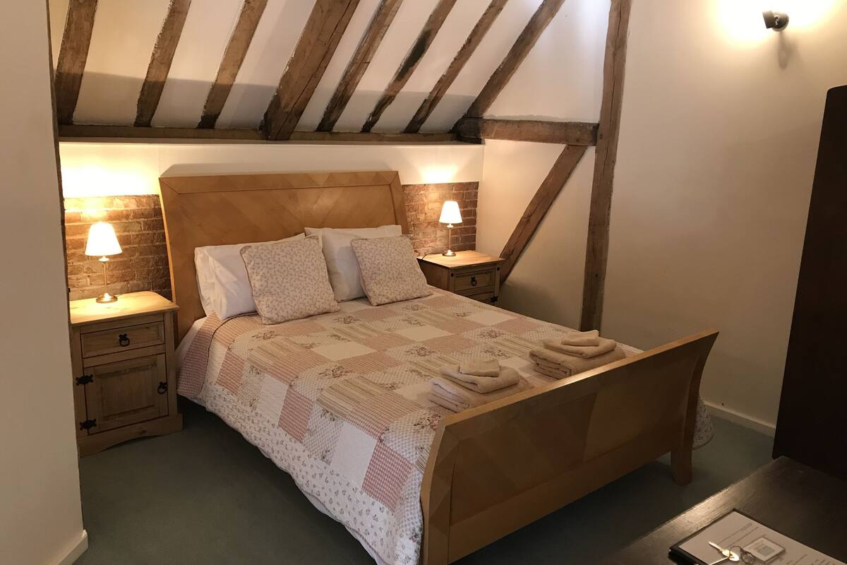 A bedroom with a wooden bed, two bedside tables with lamps, a brick wall, and a sloped ceiling.