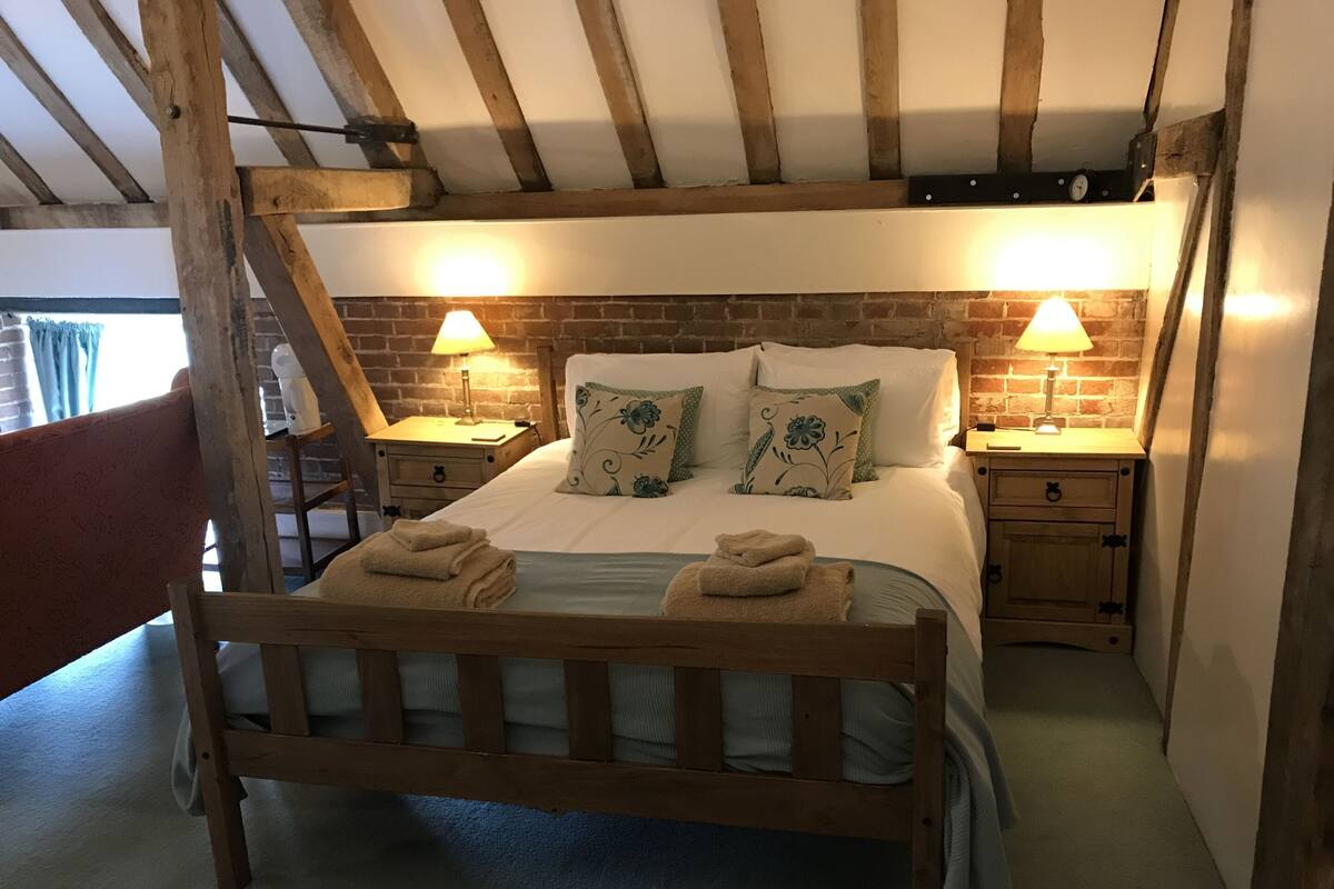 A wooden bed with two nightstands, each with a lamp, in a room with exposed beams and brick walls.