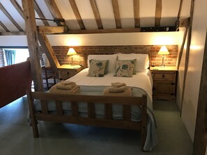 A wooden bed with two nightstands, each with a lamp, in a room with exposed beams and brick walls.