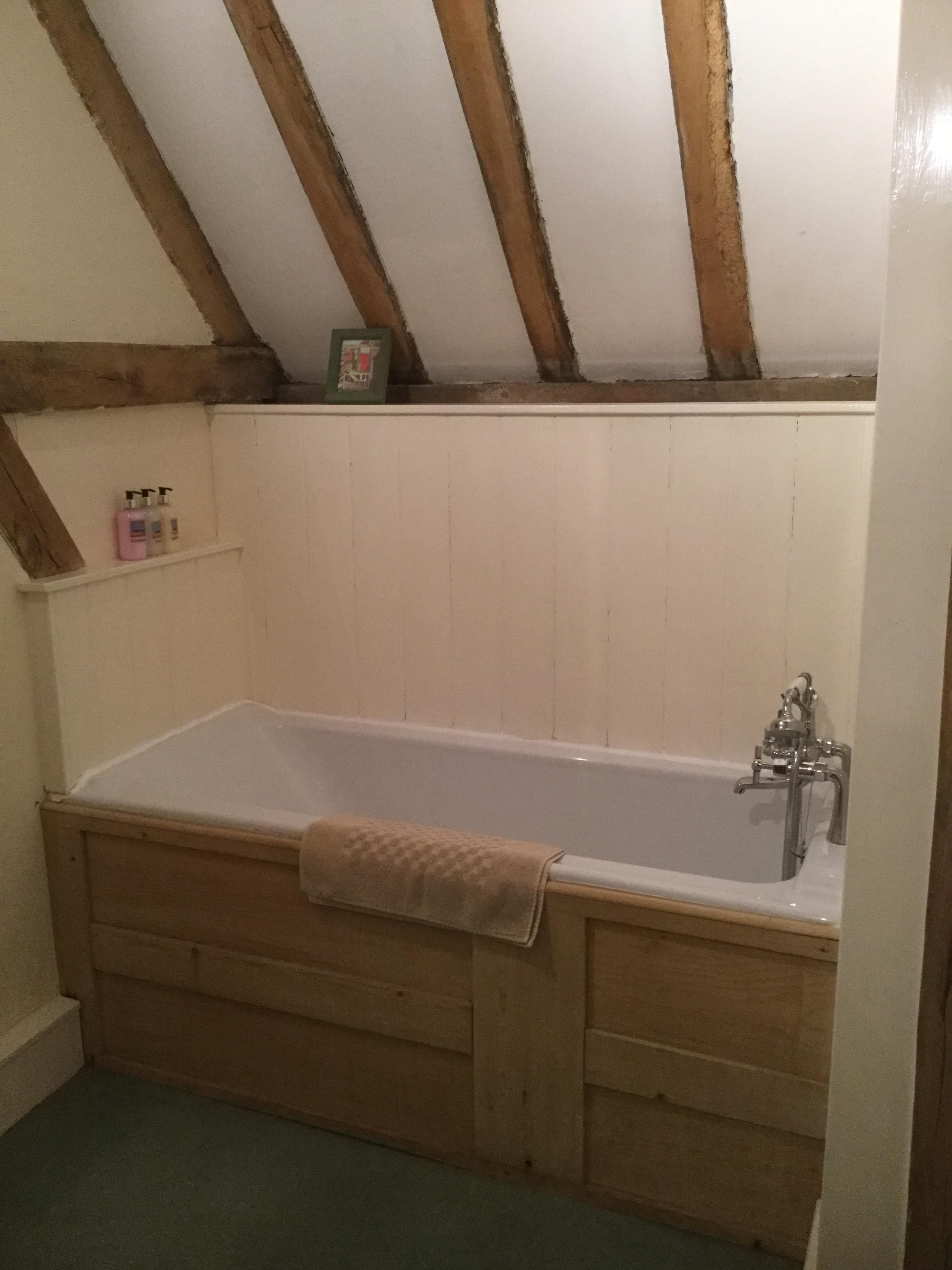 Un baño con una bañera de madera, una toalla colgada a un lado y un estante con artículos de aseo.