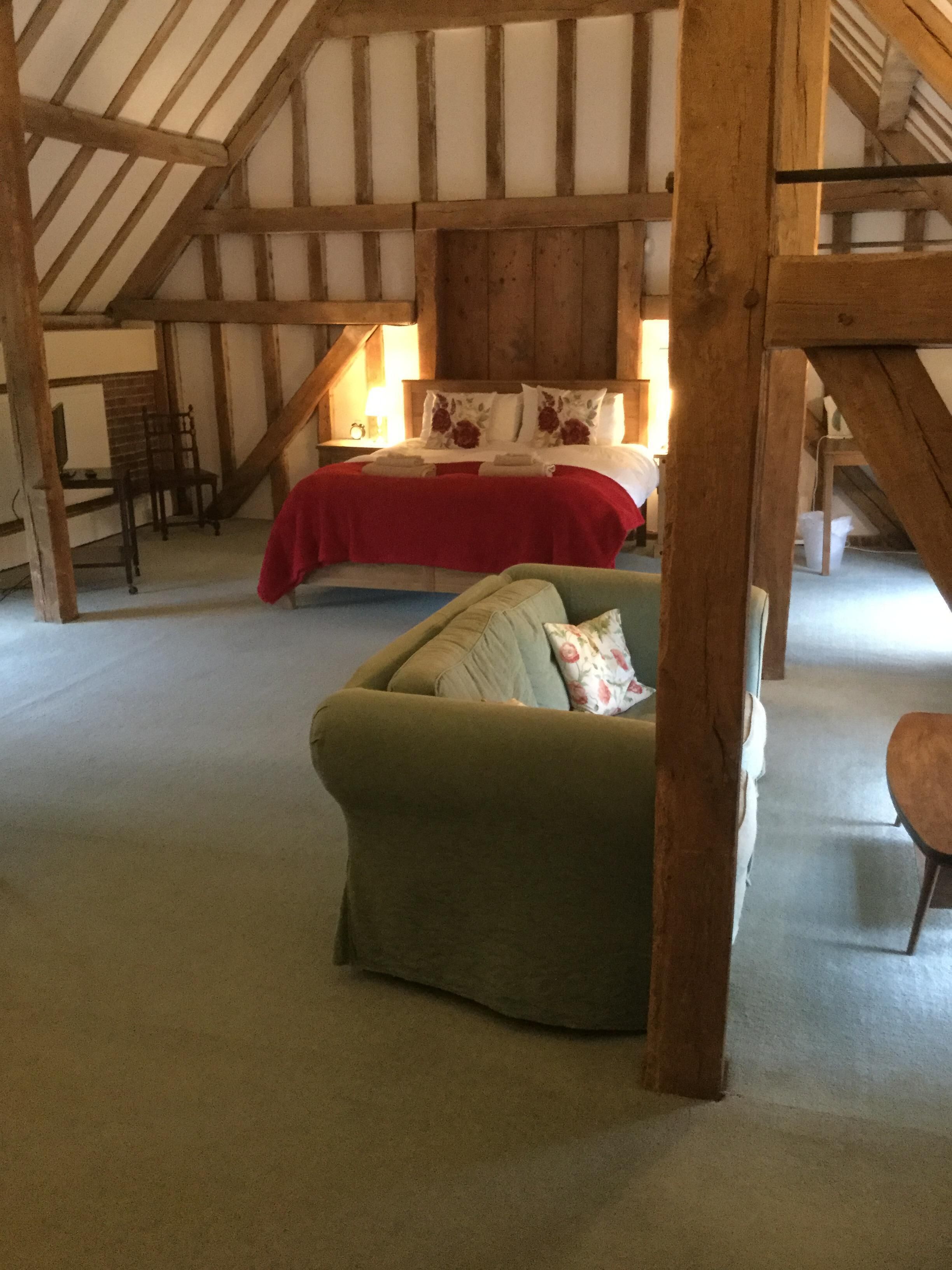 A cozy attic bedroom with a bed, a green sofa, and a wooden staircase.