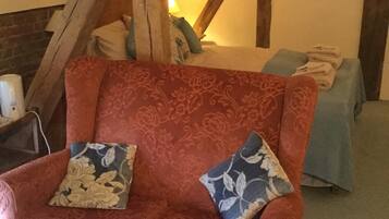 Un sofá rojo con estampado, dos cojines decorativos, una cama azul con manta a juego y un techo de madera.
