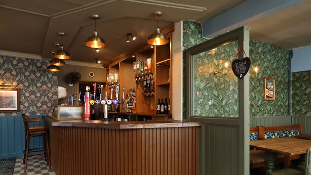 A bar area with a wooden counter, bar stools, and a variety of bottles and glasses. - The Victoria Hotel (Burnham-on-Sea)
