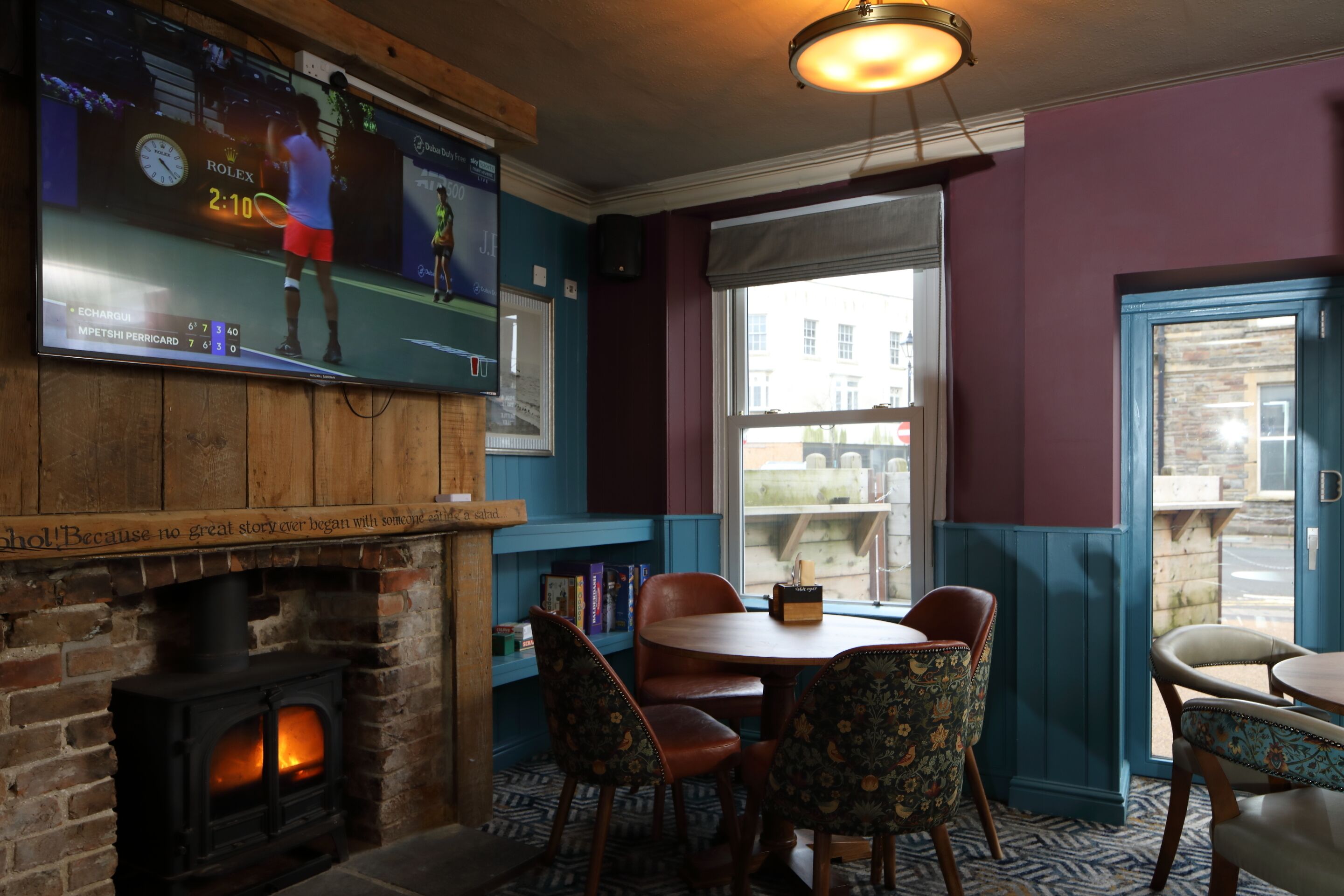 A cozy room with a fireplace, a television displaying a tennis match, and a window with a view of the street.