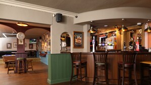 A bar area with wooden bar stools, a green partition, and a clock on the wall. - The Victoria Hotel (Burnham-on-Sea)