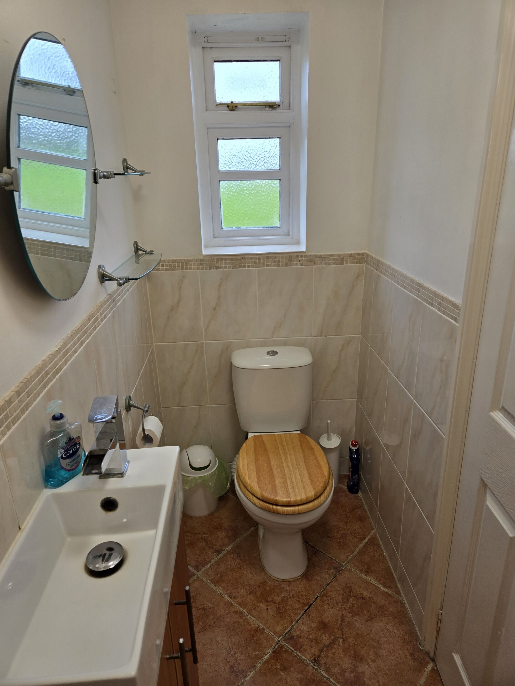 A bathroom with a toilet, sink, mirror, and window.
