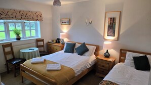 A well-lit bedroom with a double bed, a bedside table, a chair, a small table, and a window with a view of greenery. - Wayside (Norwich)